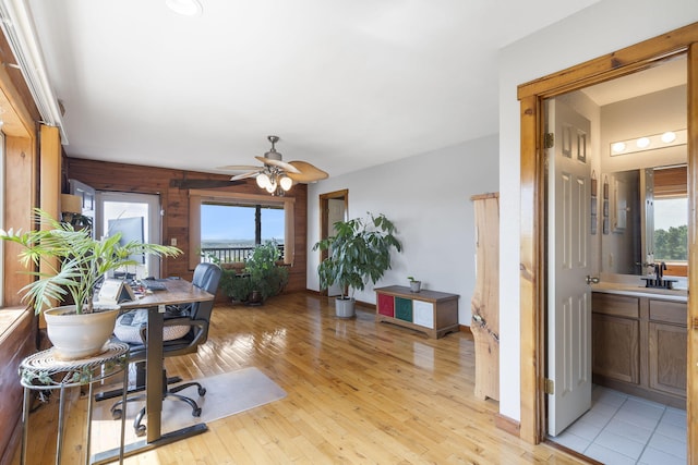 office space featuring wooden walls, sink, light wood-type flooring, and ceiling fan