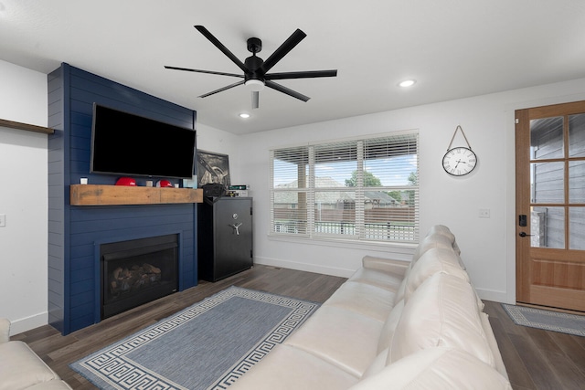 living room featuring ceiling fan, a fireplace, and dark wood-type flooring