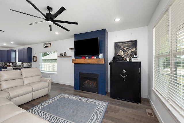 living room with ceiling fan, dark hardwood / wood-style flooring, and a large fireplace