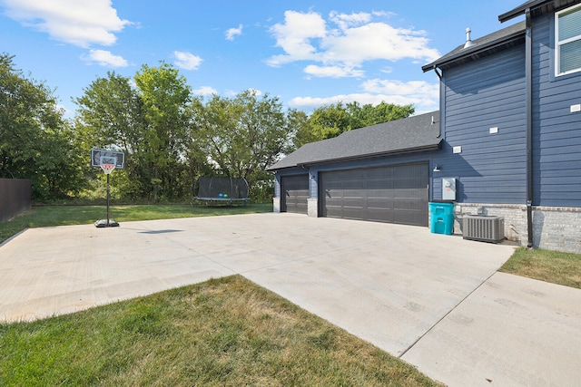 exterior space featuring a yard, central air condition unit, a trampoline, and a garage