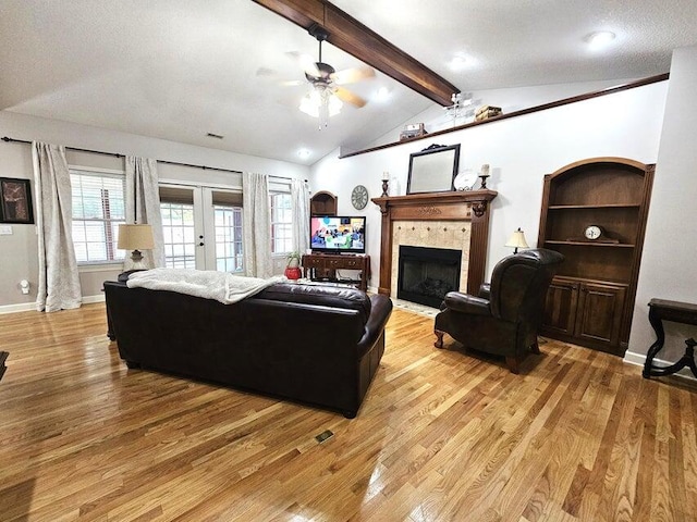 living room with ceiling fan, a textured ceiling, lofted ceiling with beams, a tile fireplace, and light hardwood / wood-style floors