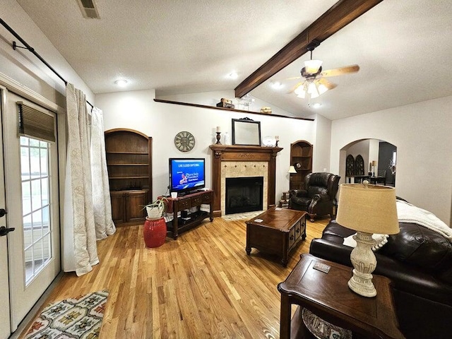 living room featuring ceiling fan, vaulted ceiling with beams, a textured ceiling, a tile fireplace, and hardwood / wood-style floors