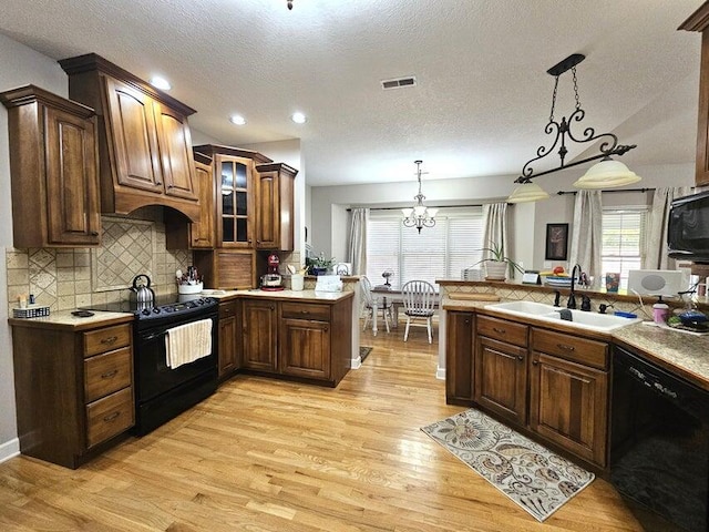 kitchen with black appliances, sink, light hardwood / wood-style floors, pendant lighting, and an inviting chandelier