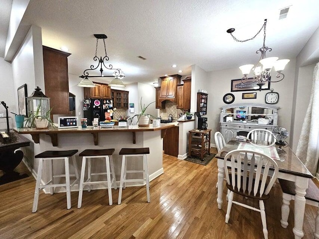 kitchen featuring an inviting chandelier, light hardwood / wood-style flooring, black refrigerator, and kitchen peninsula