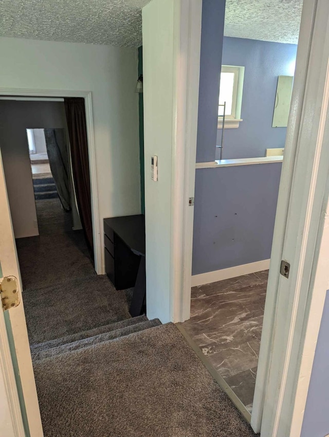 corridor featuring dark colored carpet and a textured ceiling