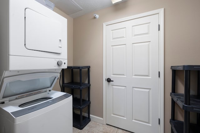 washroom featuring stacked washer and dryer, light tile patterned floors, and a textured ceiling