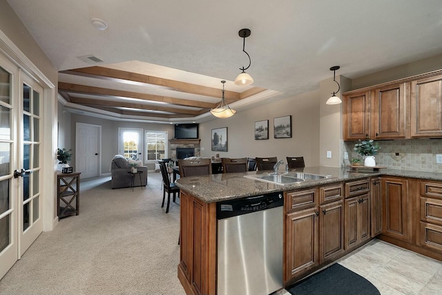 kitchen with a stone fireplace, sink, hanging light fixtures, stainless steel dishwasher, and kitchen peninsula