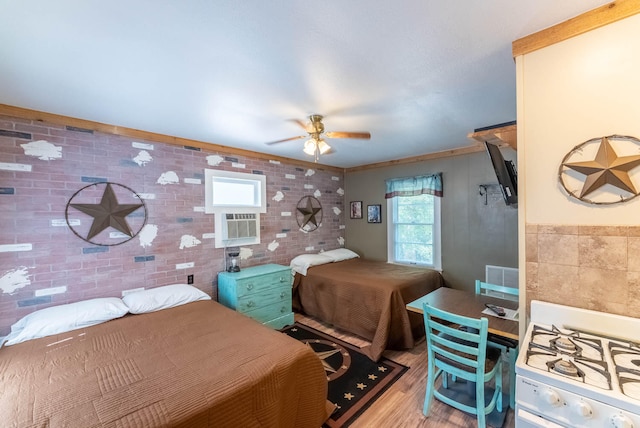 bedroom with light wood-type flooring, crown molding, ceiling fan, and brick wall