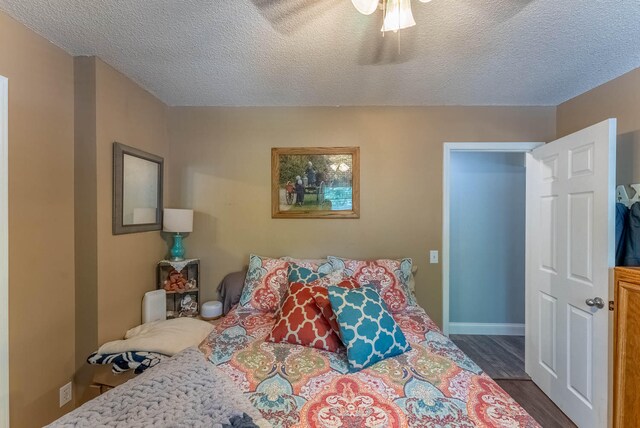 bedroom with ceiling fan, a textured ceiling, and dark wood-type flooring