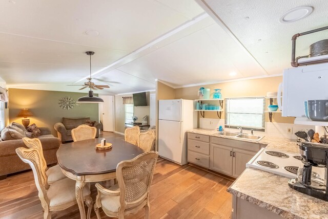 dining area with ceiling fan, lofted ceiling, ornamental molding, sink, and light wood-type flooring