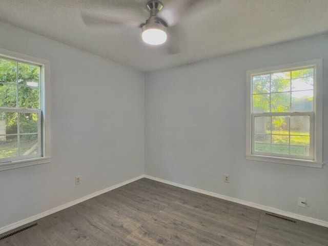 empty room featuring ceiling fan, plenty of natural light, and dark hardwood / wood-style floors