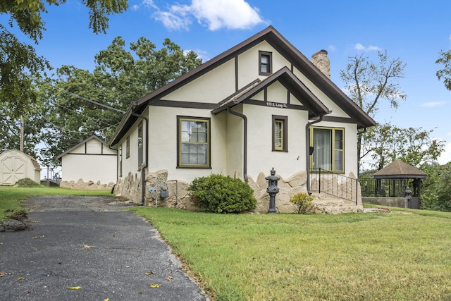 english style home featuring a front yard, a storage shed, and a gazebo