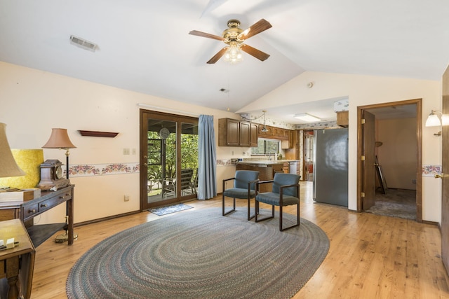 kitchen with lofted ceiling, ceiling fan, stainless steel fridge, light hardwood / wood-style flooring, and a kitchen breakfast bar