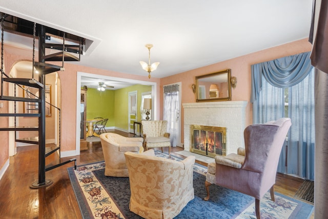 living room with dark wood-type flooring, plenty of natural light, ceiling fan with notable chandelier, and a brick fireplace