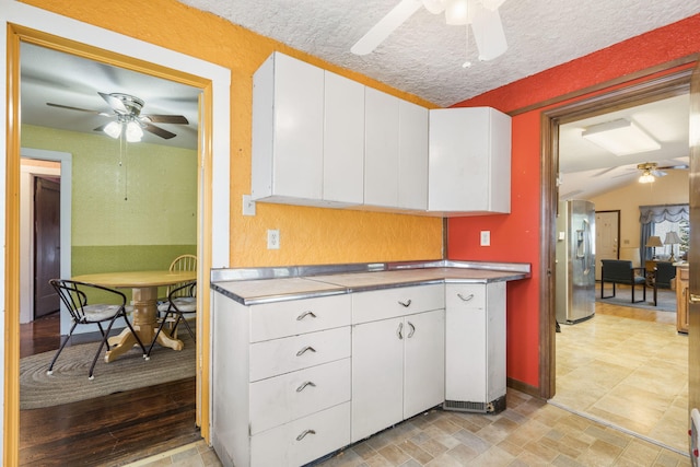 kitchen with white cabinets, vaulted ceiling, a textured ceiling, stainless steel refrigerator with ice dispenser, and light hardwood / wood-style floors