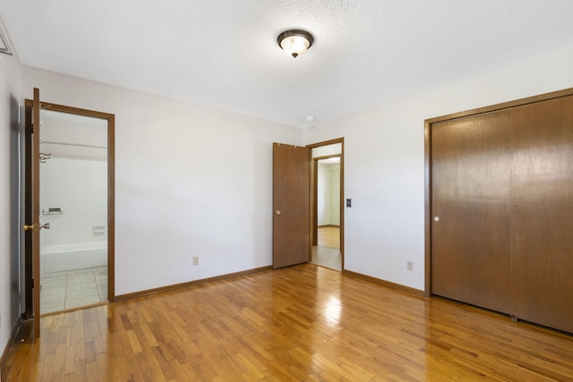 unfurnished bedroom featuring a textured ceiling, light wood-type flooring, ensuite bathroom, and a closet