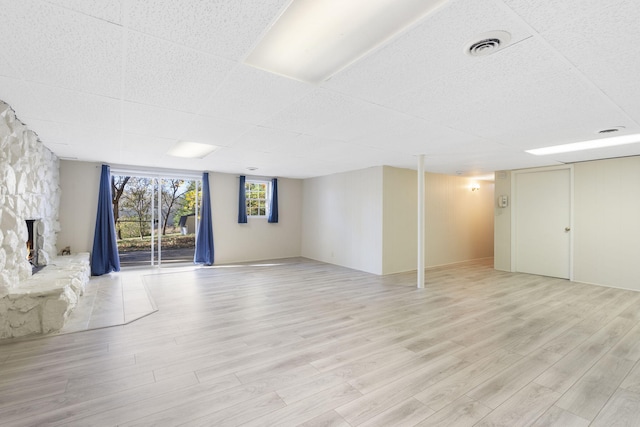 basement featuring a stone fireplace and light hardwood / wood-style flooring