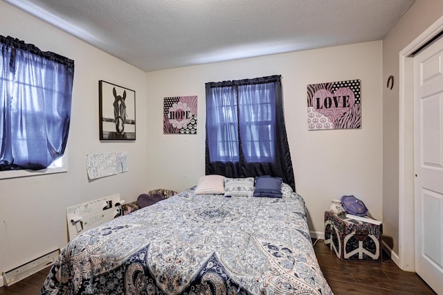 bedroom featuring multiple windows, a textured ceiling, baseboard heating, and dark wood-style flooring