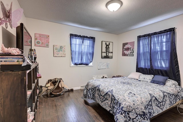 bedroom with baseboard heating, dark wood finished floors, baseboards, and a textured ceiling