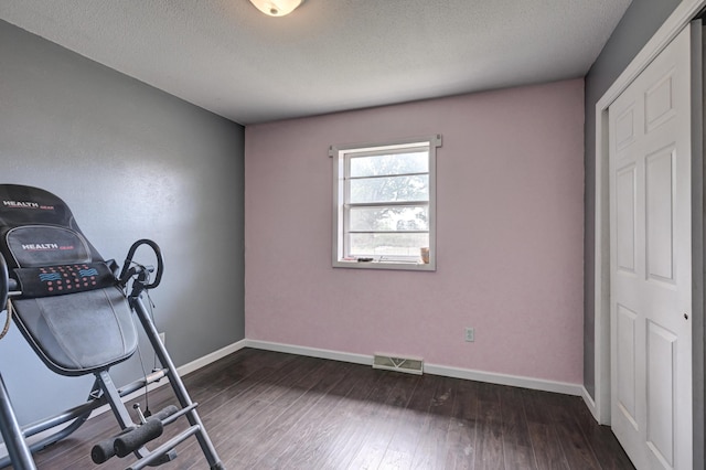 exercise room with a textured ceiling and dark wood-type flooring