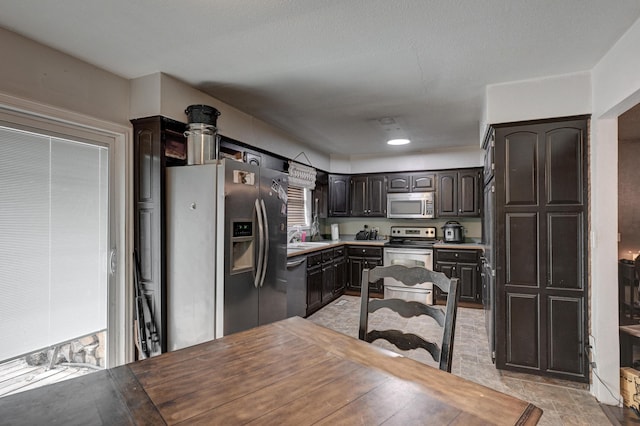 kitchen with a sink, dark brown cabinetry, light countertops, appliances with stainless steel finishes, and stone finish floor