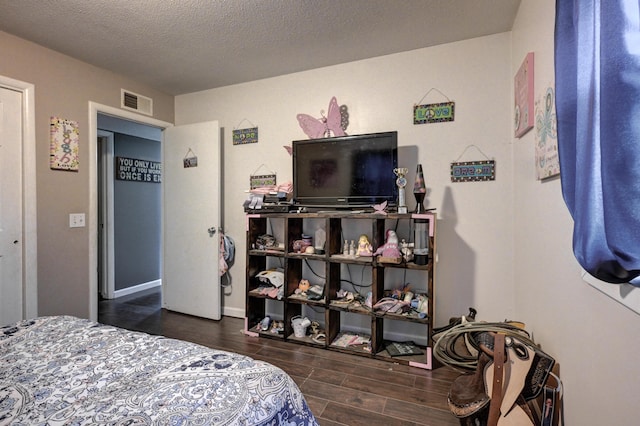 bedroom with a textured ceiling, wood finished floors, visible vents, and baseboards