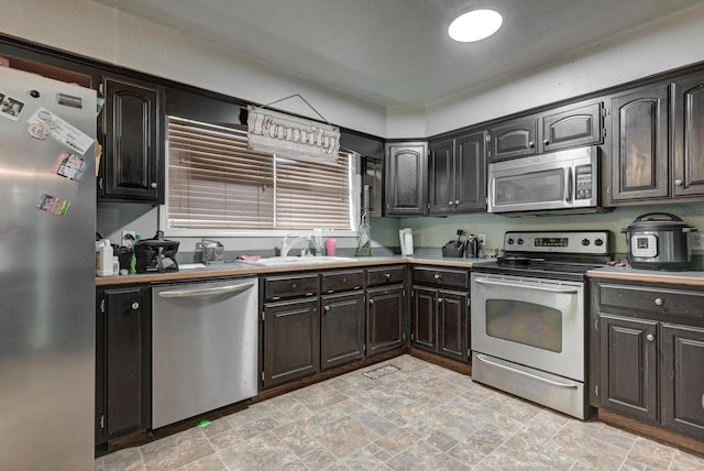 kitchen featuring stainless steel appliances, light countertops, stone finish floor, and a sink