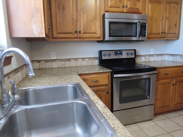 kitchen featuring light stone counters, sink, light tile patterned floors, and stainless steel appliances