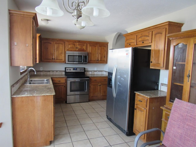 kitchen with light stone countertops, appliances with stainless steel finishes, sink, a notable chandelier, and light tile patterned flooring