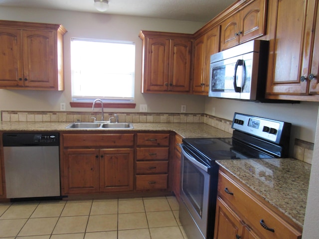 kitchen with light tile patterned floors, stainless steel appliances, light stone counters, and sink