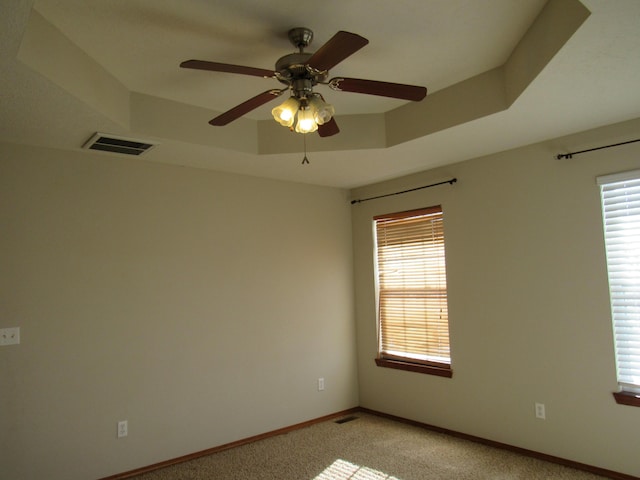 carpeted empty room with ceiling fan and a raised ceiling