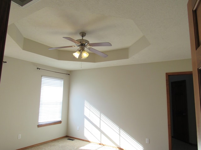 carpeted empty room with a raised ceiling and ceiling fan