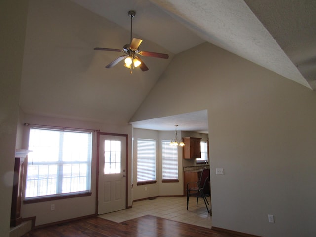 foyer entrance with a textured ceiling, ceiling fan with notable chandelier, light hardwood / wood-style flooring, and lofted ceiling