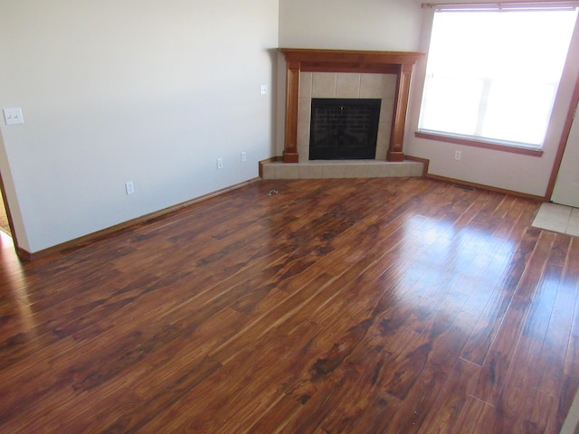 unfurnished living room featuring a tile fireplace and dark wood-type flooring