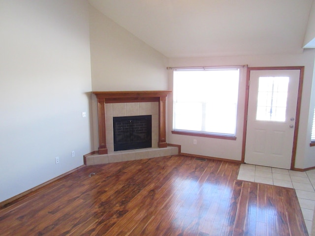 unfurnished living room featuring light hardwood / wood-style floors, a tile fireplace, and vaulted ceiling