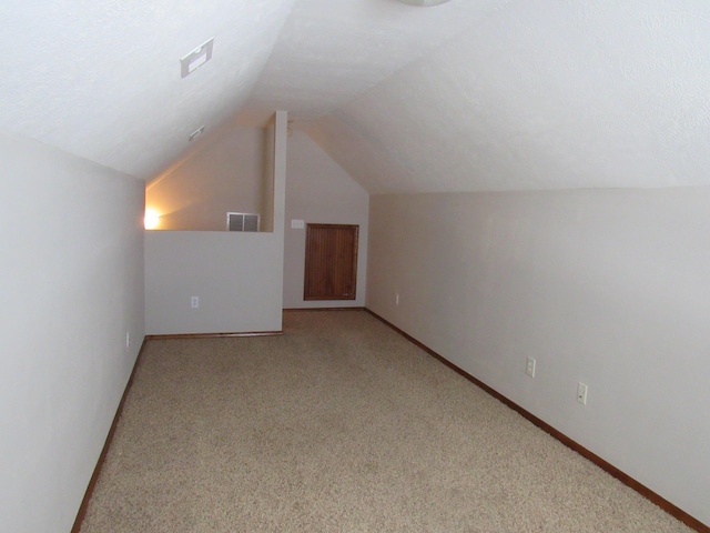 bonus room with a textured ceiling, lofted ceiling, and light carpet