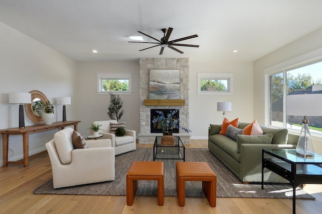 living room featuring a stone fireplace, light wood-type flooring, and ceiling fan