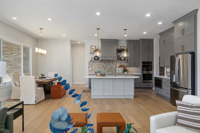 kitchen featuring appliances with stainless steel finishes, light hardwood / wood-style flooring, an island with sink, and pendant lighting