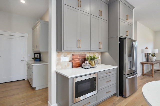 kitchen featuring gray cabinetry, stainless steel appliances, light wood-type flooring, and tasteful backsplash