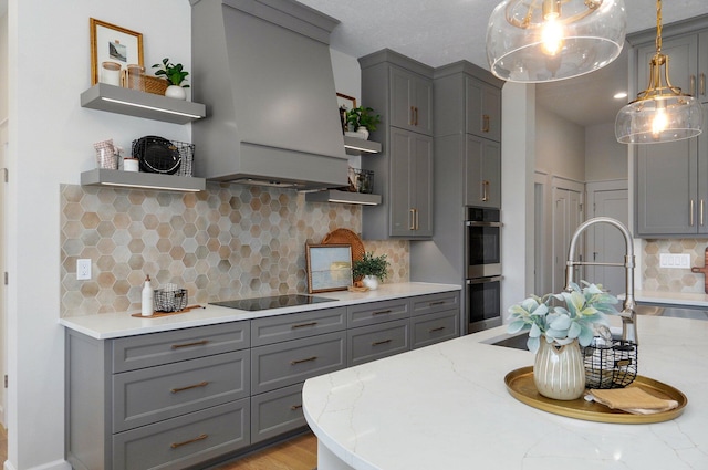 kitchen with light stone countertops, black electric cooktop, hanging light fixtures, decorative backsplash, and premium range hood