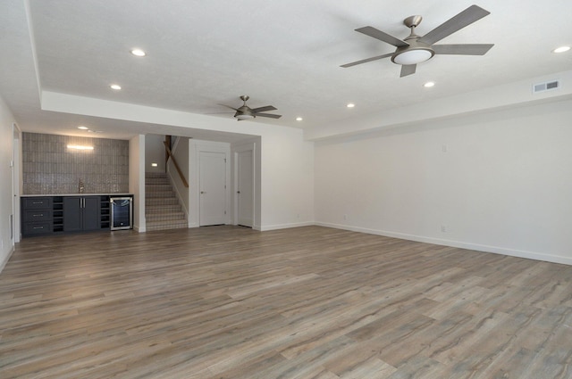 unfurnished living room with bar, wood-type flooring, and ceiling fan