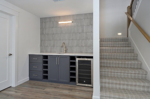 bar featuring light wood-type flooring, beverage cooler, tile walls, and gray cabinetry