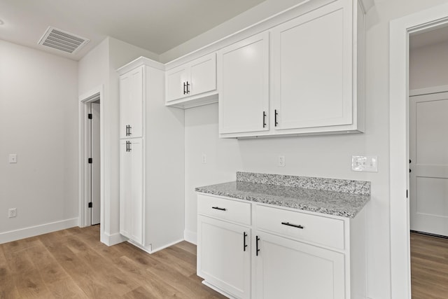 kitchen with light stone countertops, visible vents, light wood-style floors, and white cabinetry