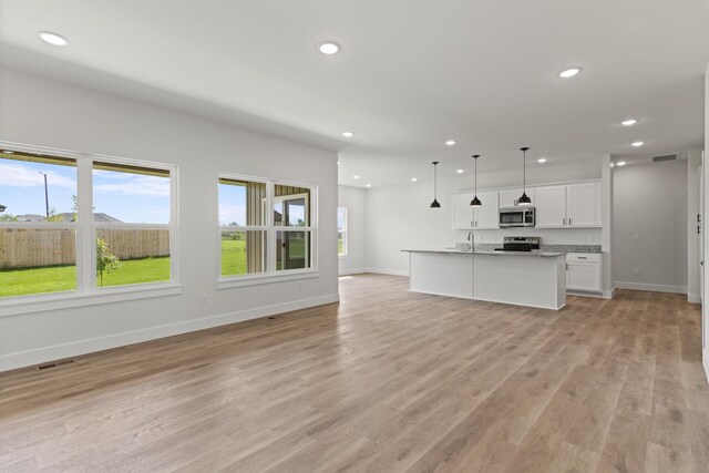 interior space with a kitchen island with sink, pendant lighting, light hardwood / wood-style flooring, white cabinets, and appliances with stainless steel finishes