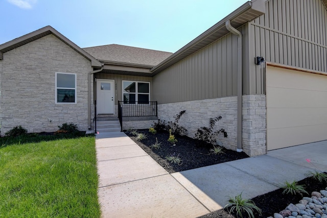 entrance to property featuring an attached garage, covered porch, stone siding, a lawn, and roof with shingles