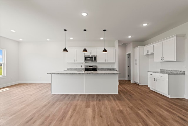 kitchen featuring light stone countertops, white cabinets, appliances with stainless steel finishes, and decorative light fixtures