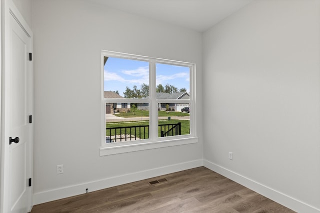spare room with wood finished floors, visible vents, and baseboards