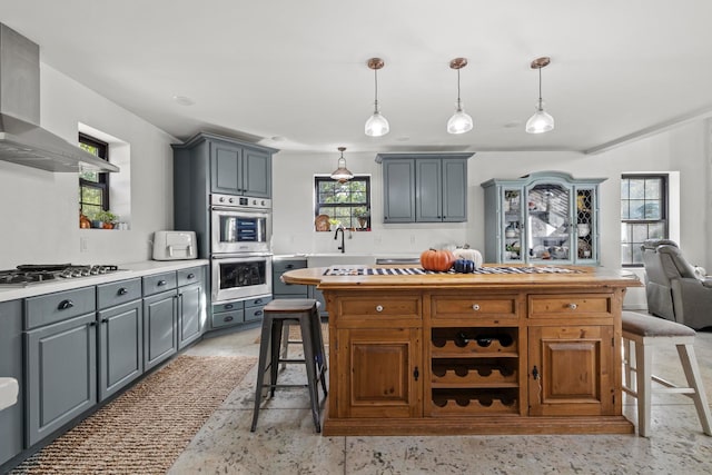 kitchen featuring appliances with stainless steel finishes, gray cabinetry, a healthy amount of sunlight, and wall chimney range hood