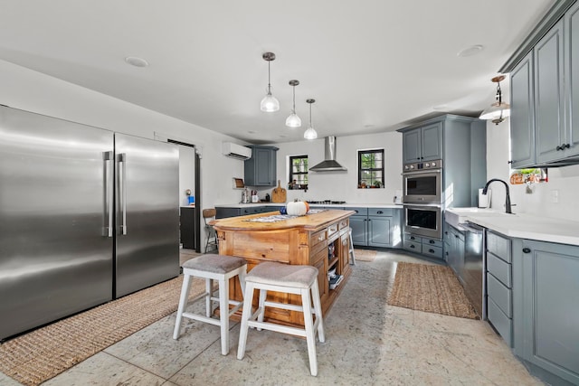 kitchen with wall chimney range hood, gray cabinetry, decorative light fixtures, a wall mounted air conditioner, and appliances with stainless steel finishes