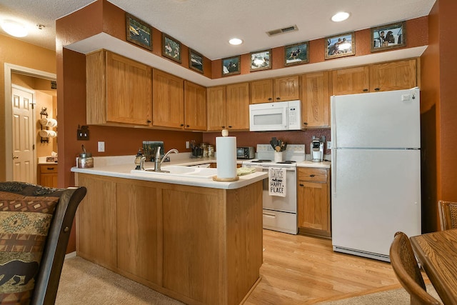 kitchen with a textured ceiling, kitchen peninsula, white appliances, and light hardwood / wood-style flooring